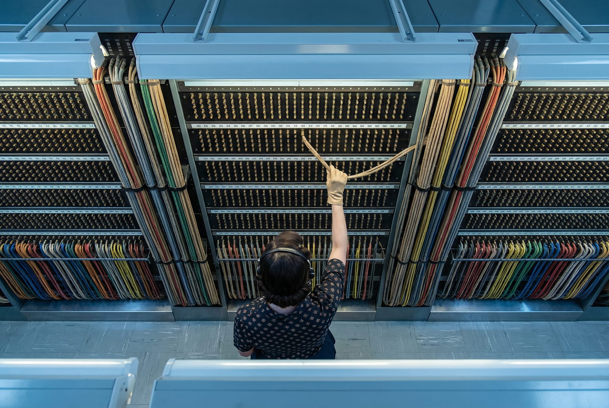 Telephone operator connecting cables on a vast numbered switchboard.